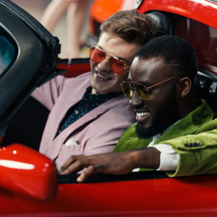 happy stylish multicultural men sitting in new car at showroom